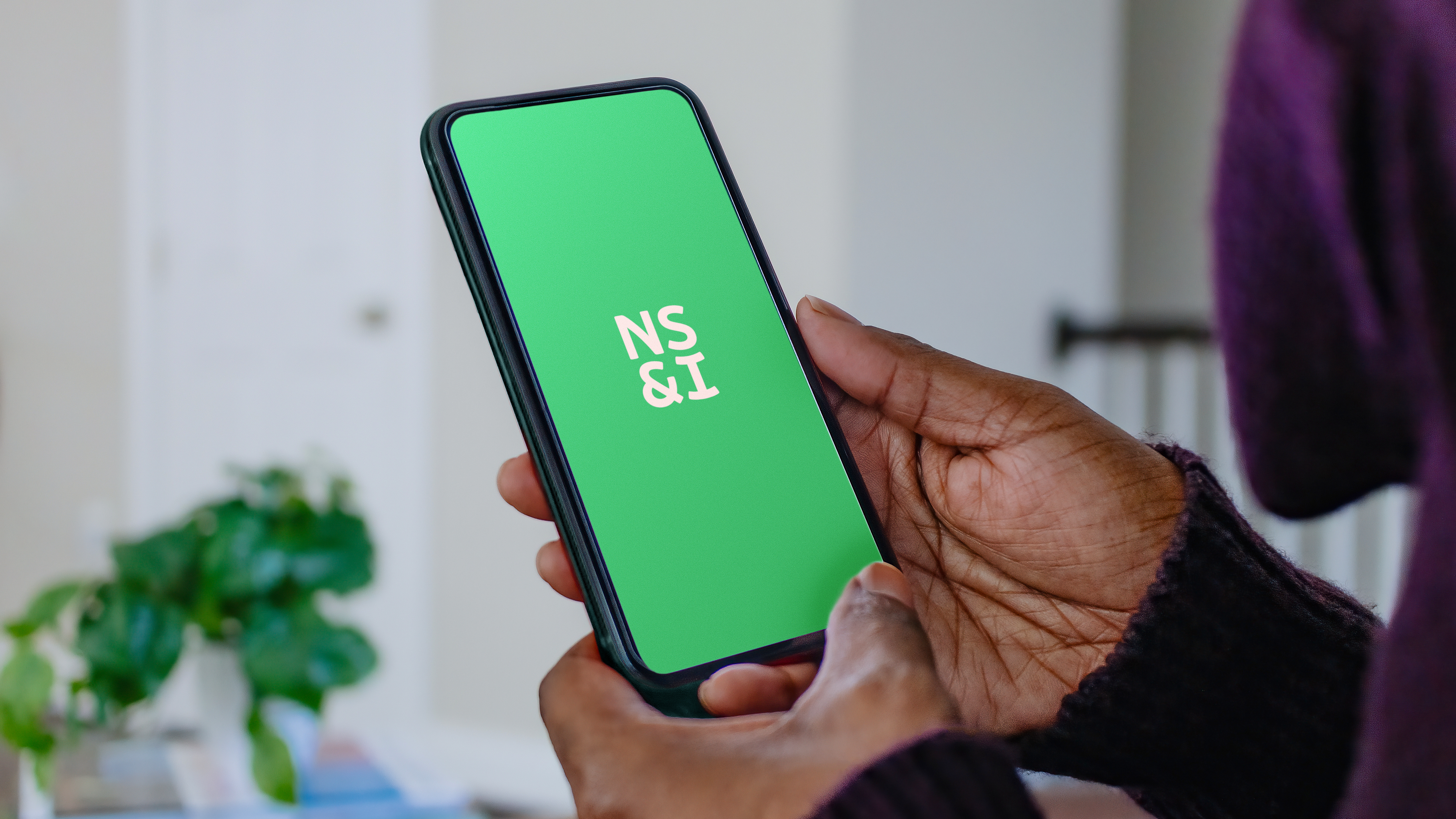 A person holding a phone with the NS&I logo showing on the screen.