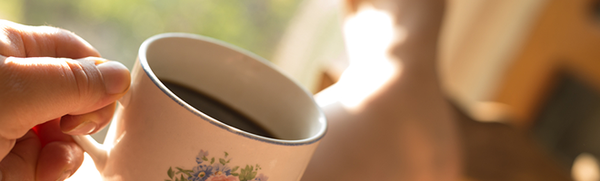 A Caucasian hand holds a mug of coffee, against a sunny background.