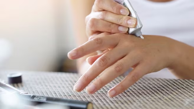 Woman applying cream from a tube to the back of her left hand.