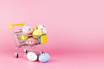 A mini shopping trolley filled with speckled, pastel Easter eggs against a bright pink background