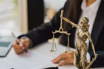 A statue of Lady Justice next to a man in a shirt and suit jacket writing on a piece of paper