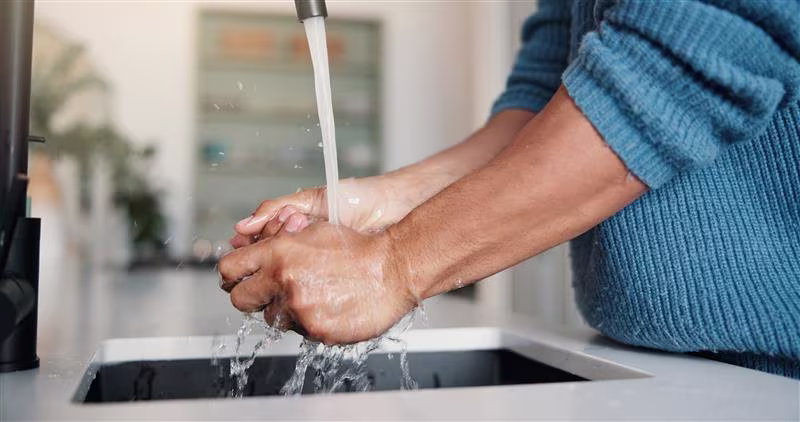 A person wearing a blue jumper washing their hands in a kitchen sink