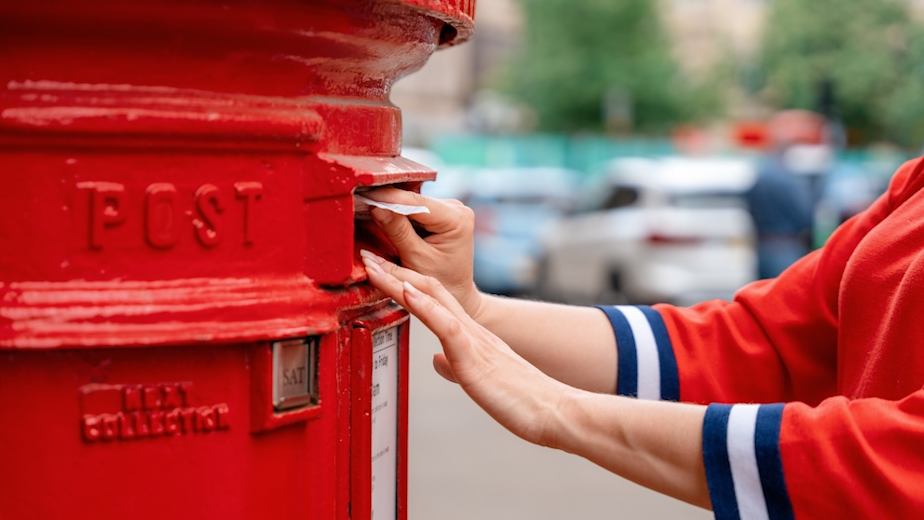 Images shows a woman posting a letter into a red postbox