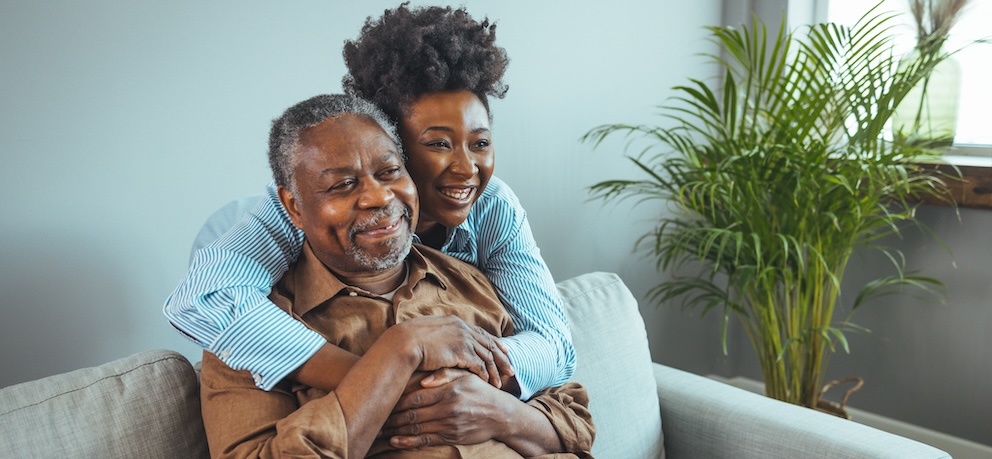 Couple hugging on the sofa – possibly a carer and their caree. 