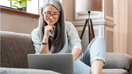 Older lady sitting on sofa looking at her laptop screen.