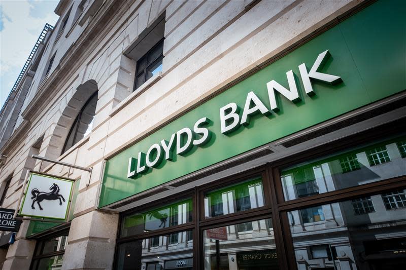 A Lloyds Bank branch exterior with the words "Lloyds Bank" on green signage and a black horse logo on a hanging sign.