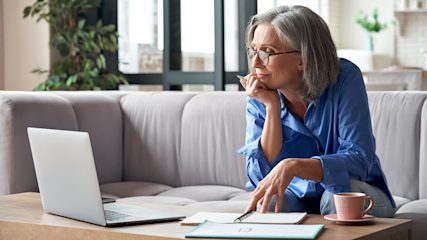 Older lady sitting on sofa with coffee and working on laptop