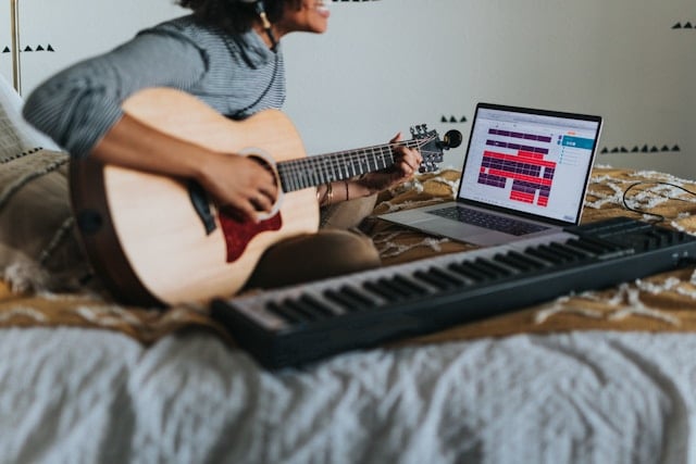Musician working on bed with guitar and laptop