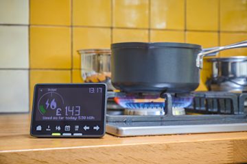 Saucepan on a turned on gas hob in a kitchen, with an in-home energy device in front of it.