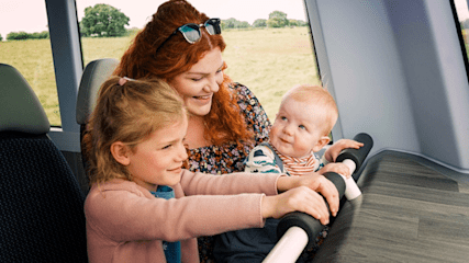 A woman and two children sitting on a bus, smiling