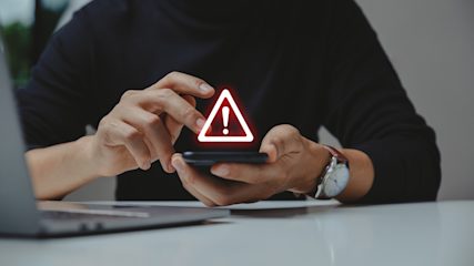 Person using smartphone with warning alert icon hovering above screen