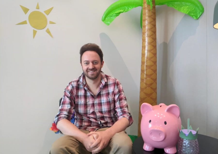 MSE Oli sits smiling beside an inflatable palm tree and a giant piggybank.