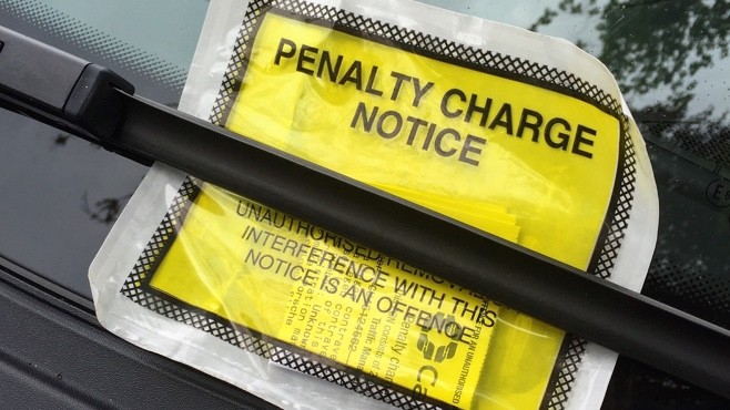 Yellow parking ticket left under a windscreen wiper, which reads "Penalty Charge Notice".