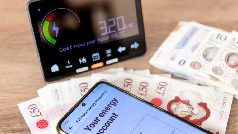 A smart meter, showing a readout of 3.2 kilowatt hours, next to two small piles of banknotes and an upturned mobile phone, which says "your energy account" on the screen.