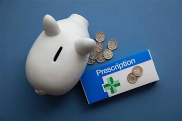 A white piggy bank, a prescription box, and a handful of pound coins against a dark blue background