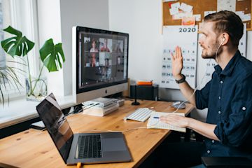 Man at desk on his laptop, which shows an on-screen call with multiple people on video