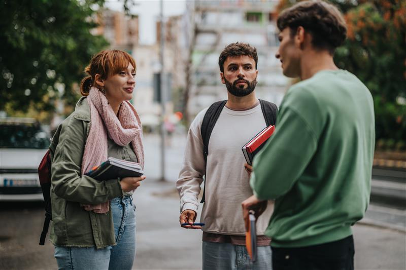 Three students standing outside holding small stacks of books and talking