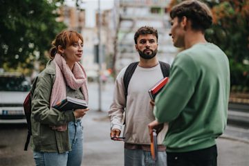 Three students standing outside holding small stacks of books and talking