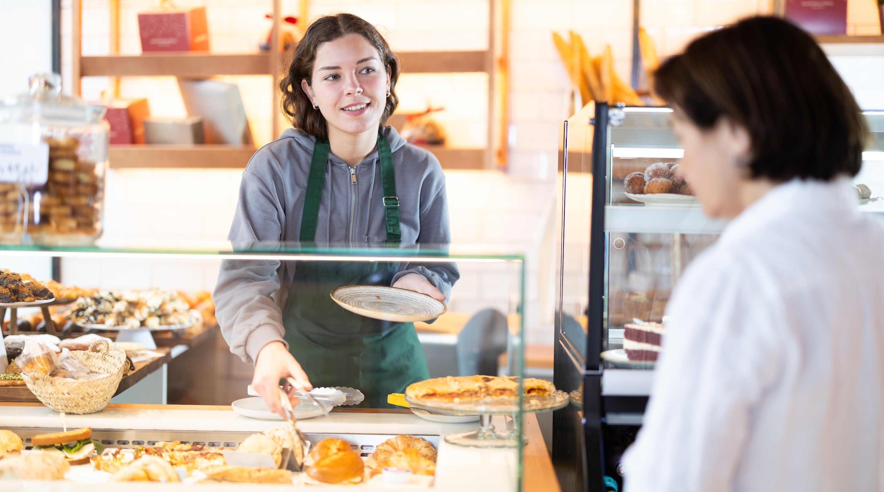 A person wearing a grey sweatshirt and green apron serving a customer at a cafe
