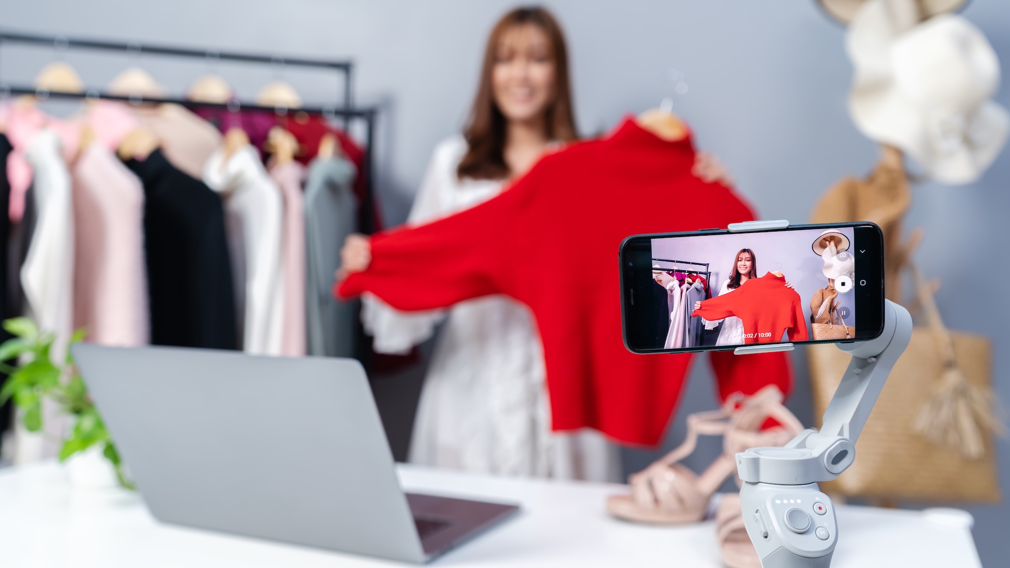 A woman taking a video of herself holding up a red jumper.