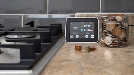 Smart meter in-home display on the kitchen side next to a gas hob and a jar of coins.