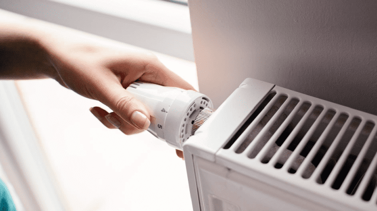 Image shows a hand turning the heating knob on a radiator.