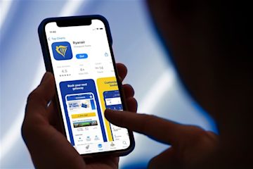 A person holding an iPhone in their hand, pointing to a description of the Ryanair app on the app store