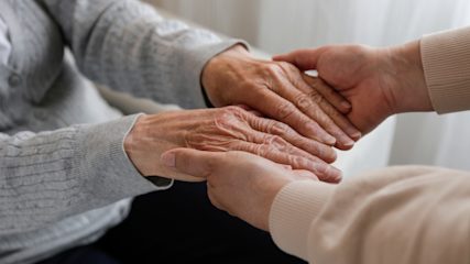 Elderly person's hands being held by someone else.
