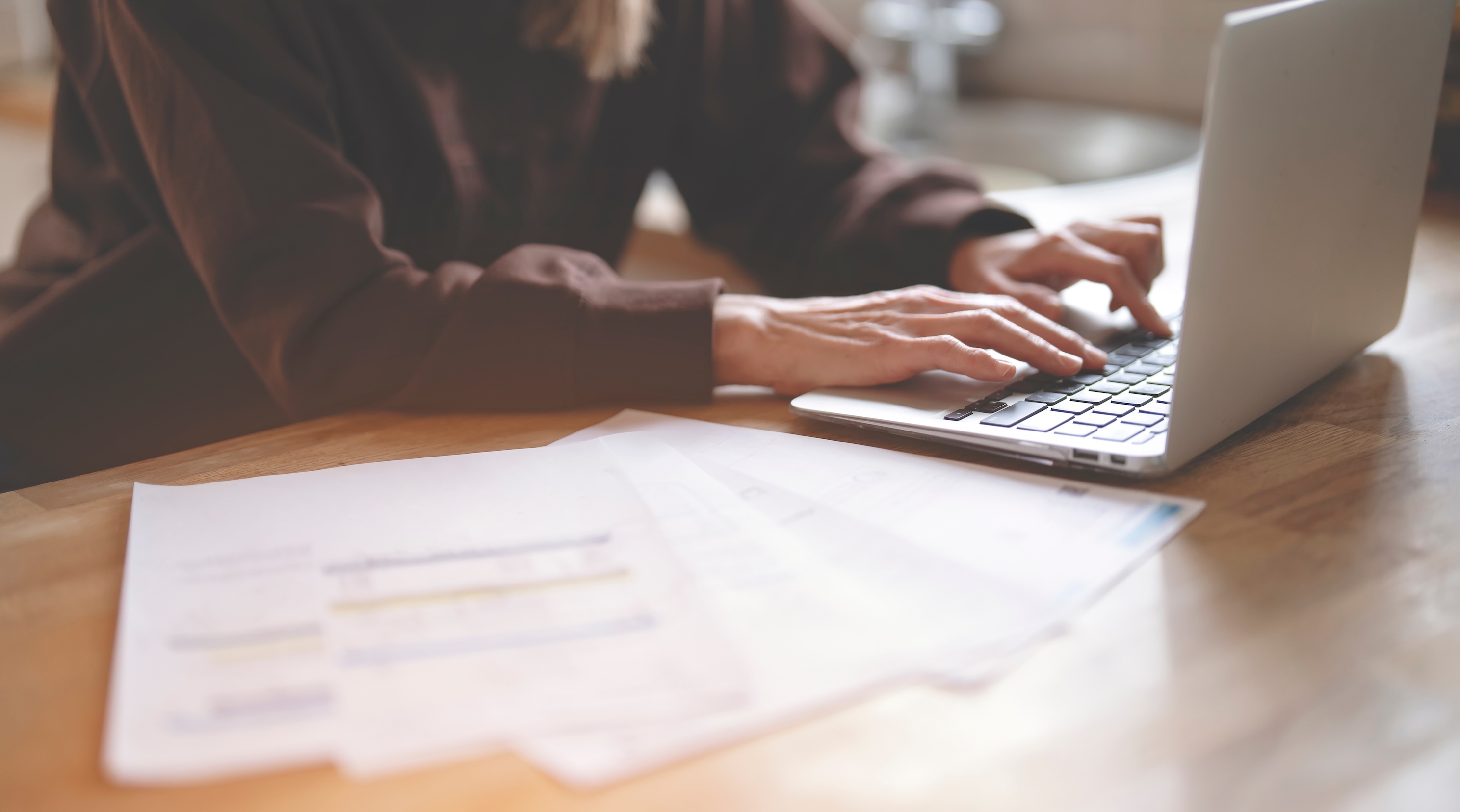 Woman working on laptop with paper documents laid out next to it 