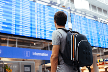 A person wearing a backpack looking at the departures board at an airport