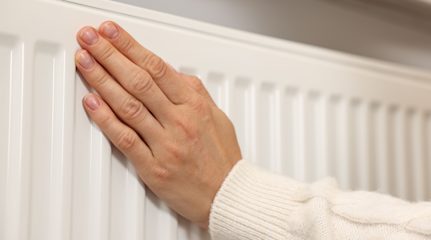 Person's hand on a radiator to feel if it's warm.