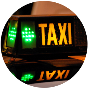 A close-up of a luminated taxi sign, showing the word TAXI in capital letters next to a green light.