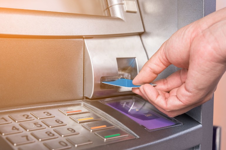 A Caucasian hand feeding a blue payment card into an ATM.