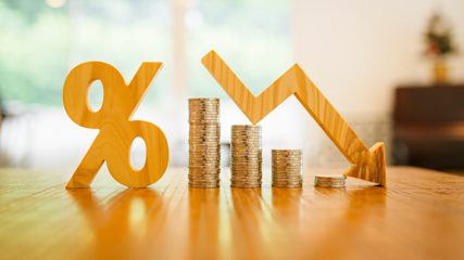 Wooden carvings of a percentage symbol and down arrow stacked with coins stacked on a tabletop
