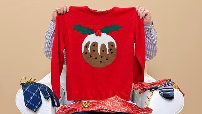 Man holding up a red jumper with a Christmas pudding on it in front of his face.