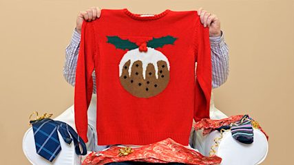 Man holding up a red jumper with a Christmas pudding on it in front of his face.