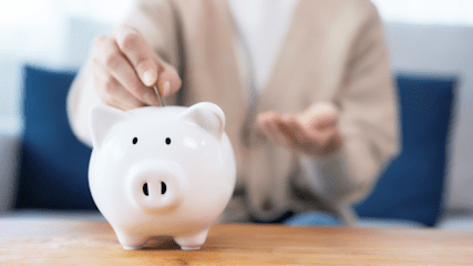 A person putting coins into a white piggy bank