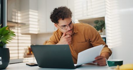 Man with laptop sitting at a kitchen table and reviewing documents.