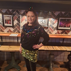 MSE Jenny H at the MSE Christmas party 2024 wearing a sparkly green skirt bought in a charity shop for £4. She also wears a black jumper with sequins around the neck, sparkly tights and has her hand on her hip