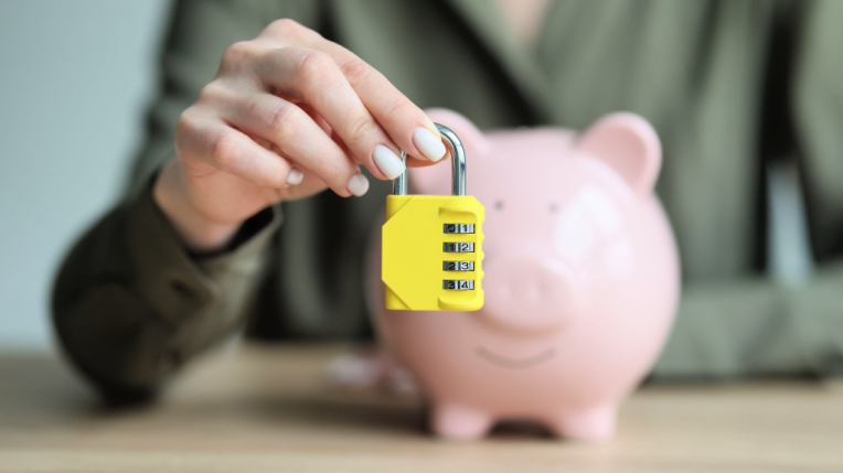 A woman holding a lock in front of a piggy bank