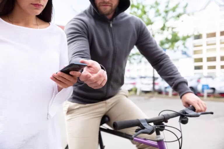 A hooded man on a bike goes to snatch a phone out of a woman's hand.