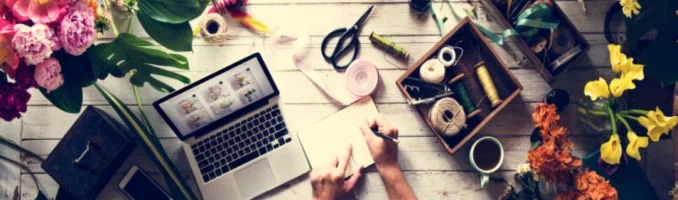 Image of somebody working on a laptop surrounded by flowers.