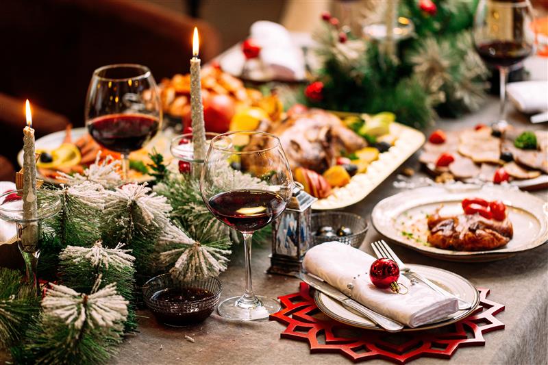 A table set for Christmas dinner, with glasses of red wine, candles and snow-dusted pine branches