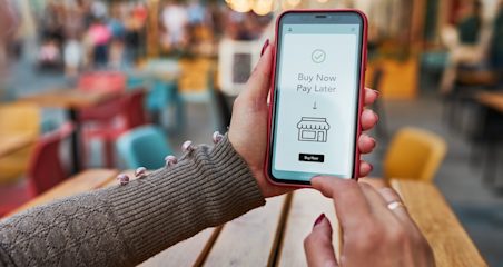 A person holding a phone that says 'Buy Now, Pay Later' with a small shop icon