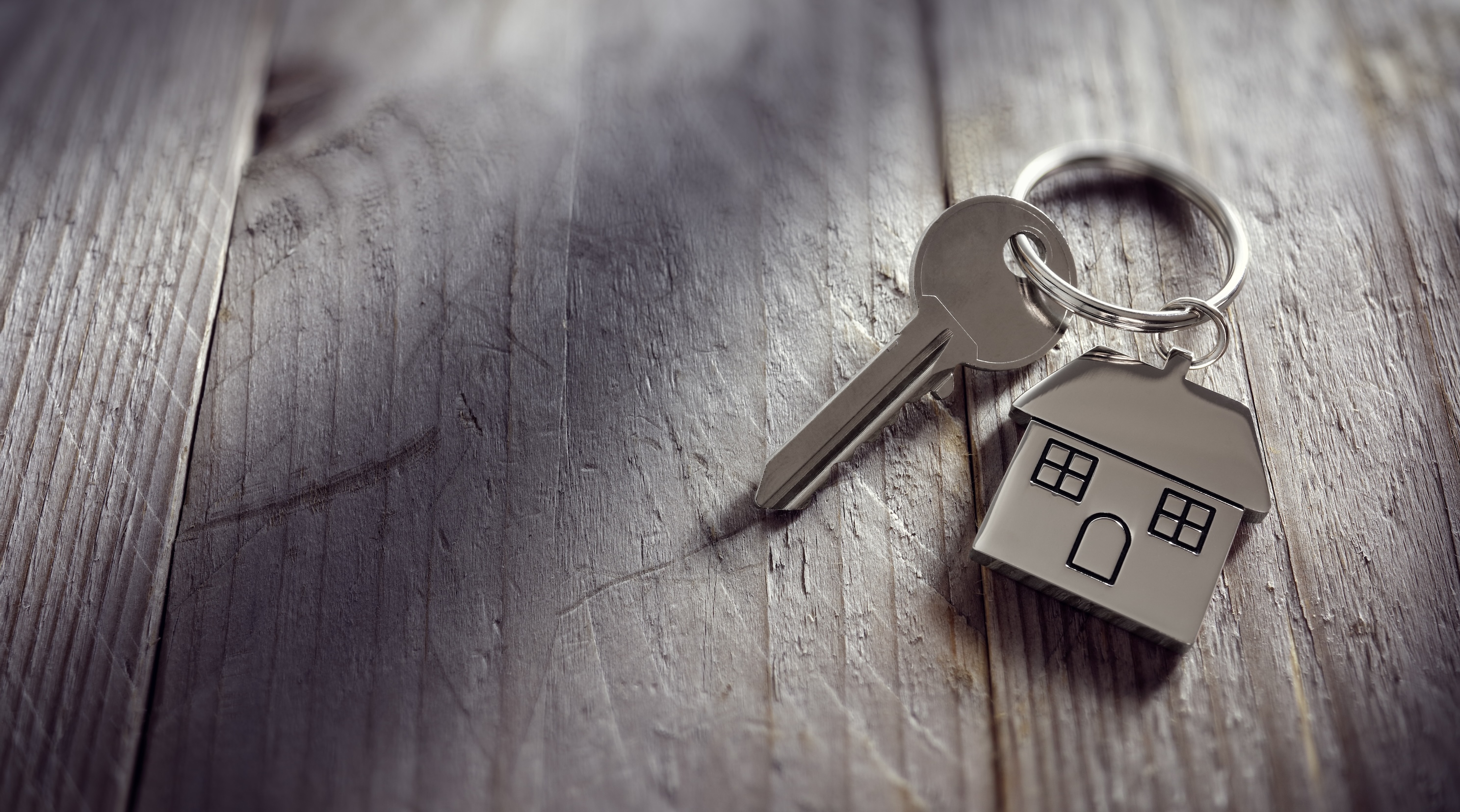 Key with house-shaped keyring against wooden table