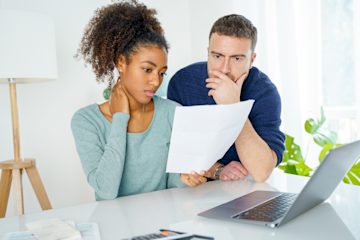 Woman and man looking anxiously at paperwork and a laptop