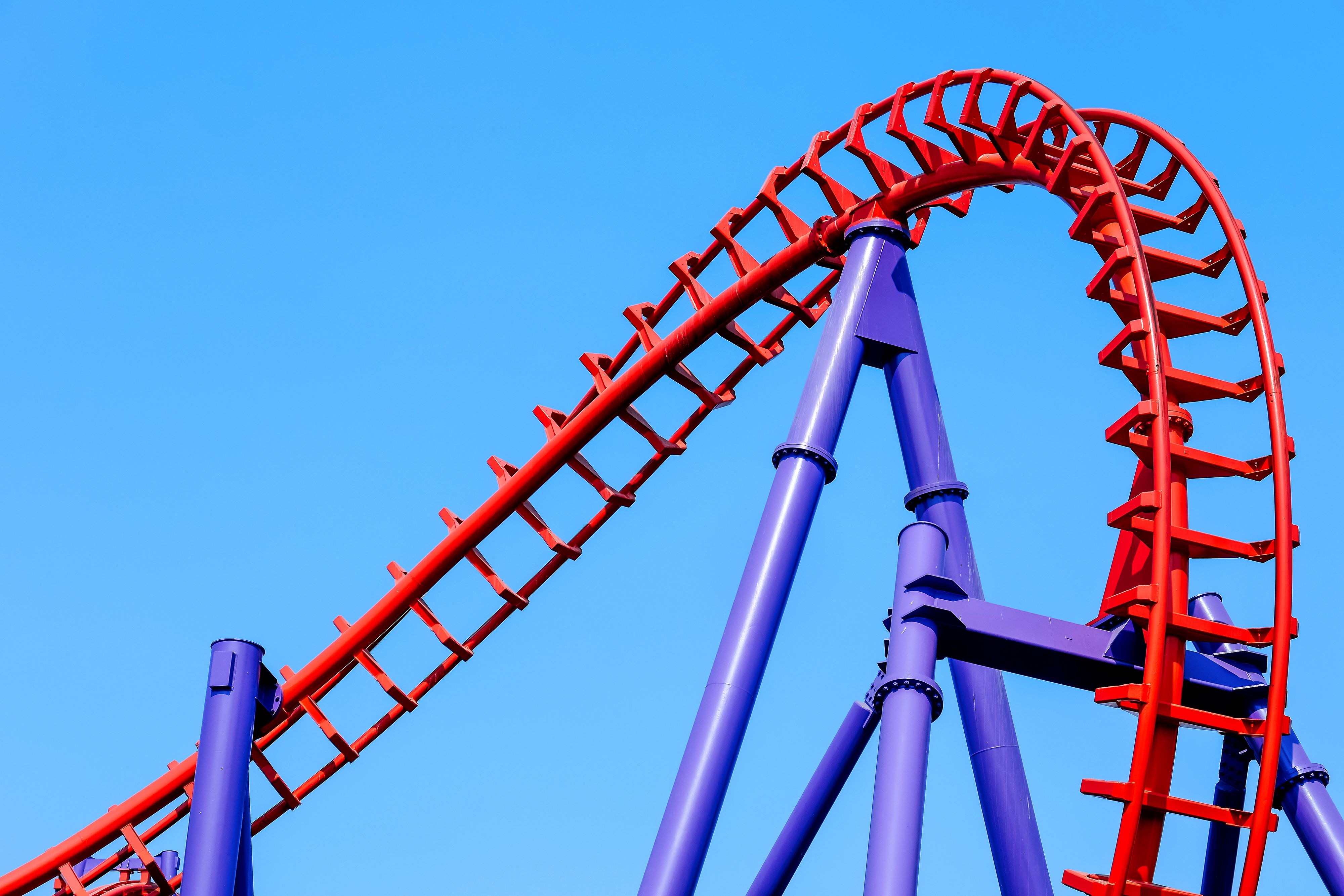 Red and purple rollercoaster tracks on a bright blue sky.