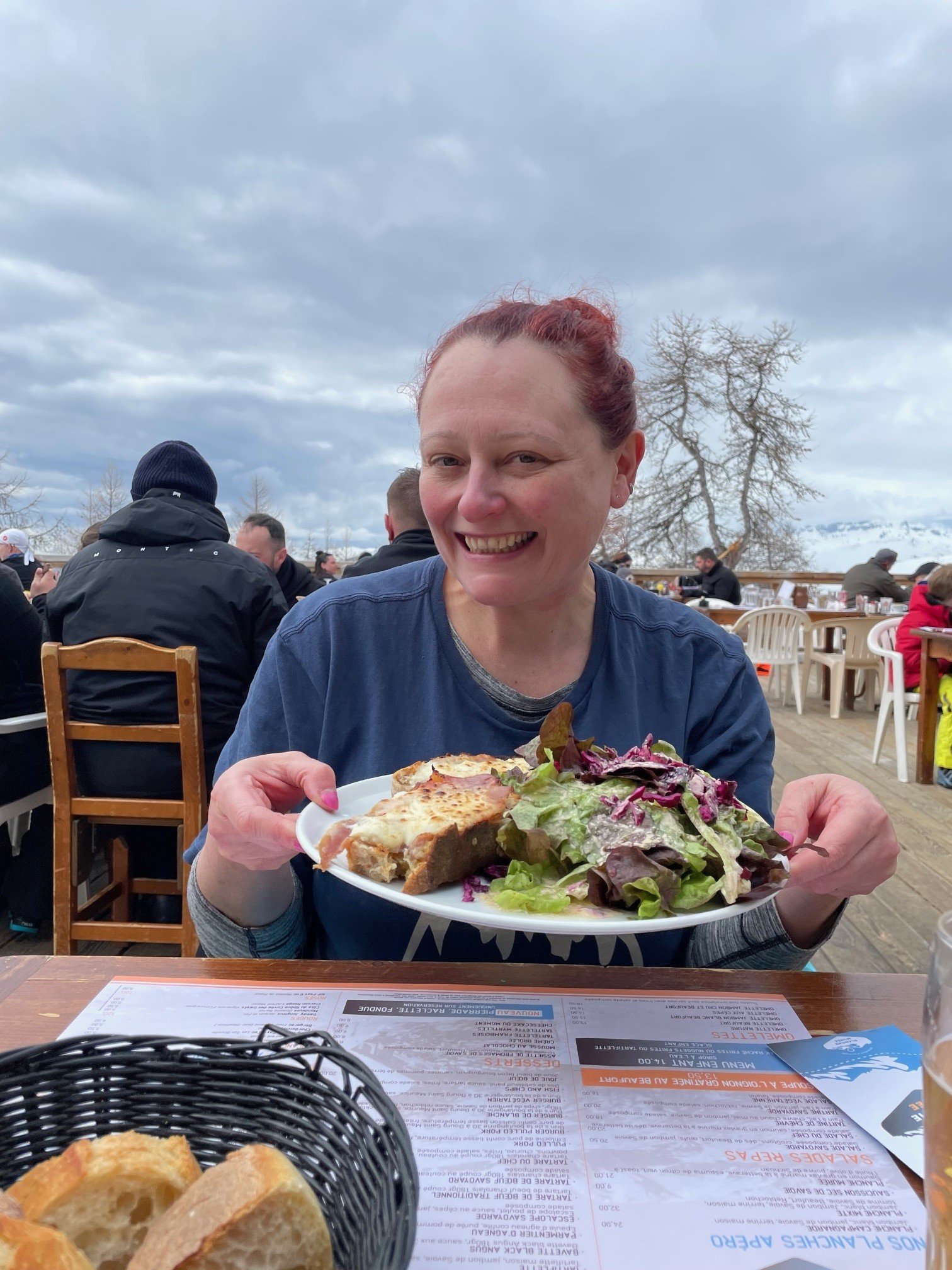 MSE Jenny H, who wrote this blog, holds up a plate of cheesy bread and salad in a mountain restaurant.