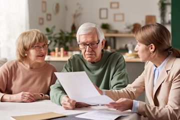 Older heterosexual couple looking through paper documents with a lady in a suit.