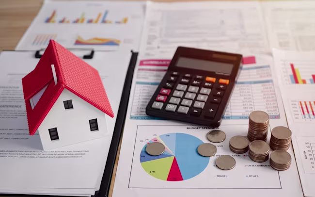 Miniature house on paper files with coins and a calculator